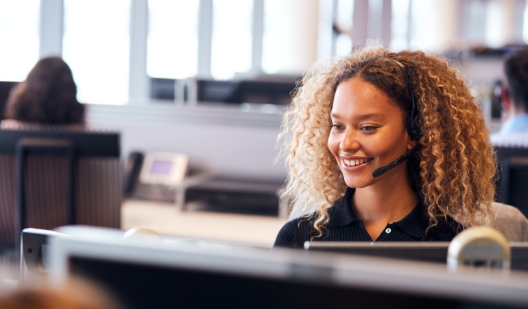 Young Businesswoman Wearing Telephone Headset Talking To Caller In Customer Services Department