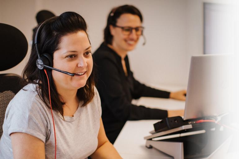 Website In-Page (770 x 512 px) Two members of Modern Networks Carrier Services team, wearing headsets and working on computers
