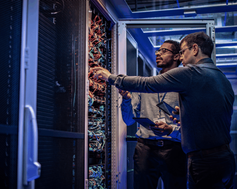 Two network engineers examine a server rack in a data centre