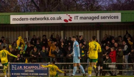 A photograph of a Hitchin Town FC football match with Modern Networks sponsorship banner in view