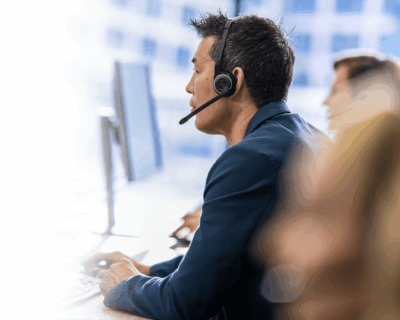  man wearing a headset and speaking to a customer while working on a computer in an office