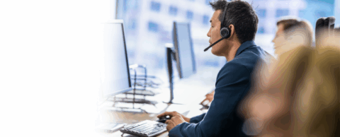  man wearing a headset and speaking to a customer while working on a computer in an office